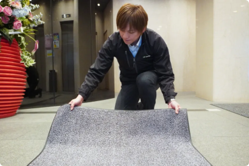 黒いジャケットの男性スタッフがビルのエントランスでグレーのマットを床に広げている様子