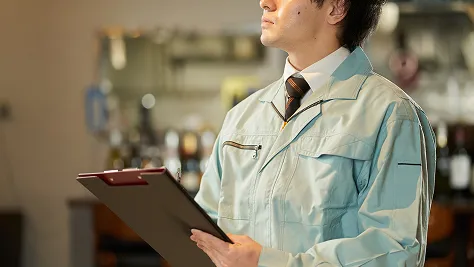 作業着を着た男性スタッフがクリップボードを持ち、店舗内を調査している様子