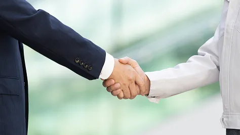スーツ姿の男性と作業着の男性が屋外で握手を交わしている様子