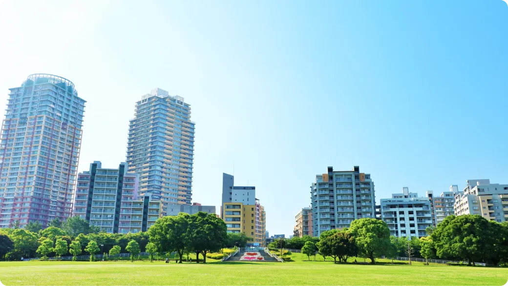 青空の下に広がる芝生の公園と、その奥に並ぶ高層マンション群の街並み