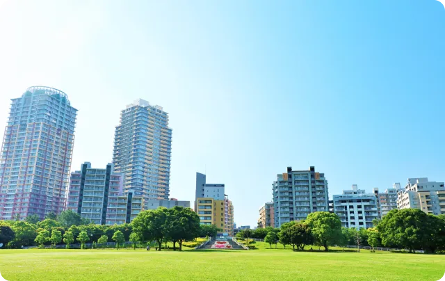 青空の下に広がる芝生の広場と、その奥に並ぶ高層マンション群の街並み
